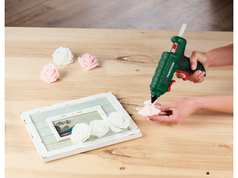 Personne utilisant un pistolet à colle chaude Parkside pour fixer des roses décoratives sur un cadre photo.