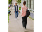 Une femme marche avec un sac à dos noir et une veste bomber rose avec un motif papillon.