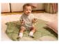 Bébé souriant assis sur un tapis vert, tenant un hochet en bois.