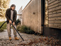 Un homme utilise un souffleur à feuilles pour enlever les feuilles d'un chemin de gravier.