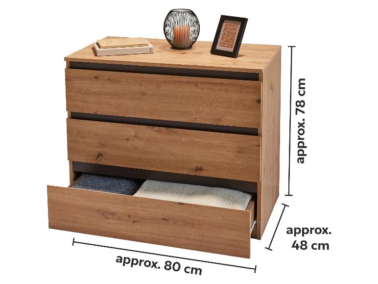 Commode en bois à trois tiroirs, un ouvert, avec une bougie et un cadre photo sur le dessus.