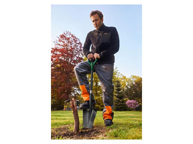 Homme en veste polaire noire et pantalon de travail orange-gris avec pelle dans le jardin.