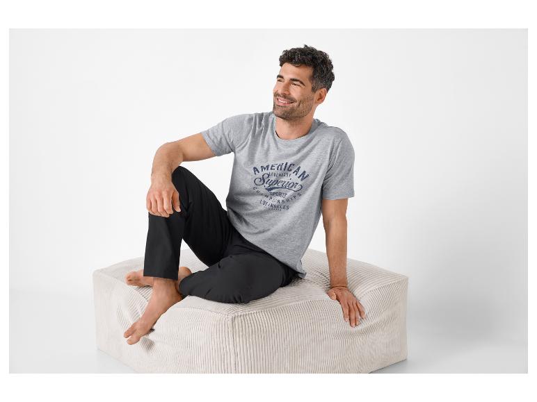 Homme en pyjama gris et noir assis sur un pouf beige.