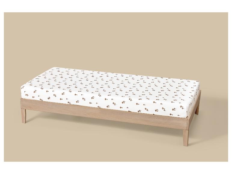Matelas à langer avec housse blanche à motif de champignons bruns, sur un cadre en bois.