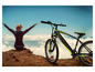 Une femme profite de la vue sur une montagne, avec un vélo électrique noir Sachsrad à côté.