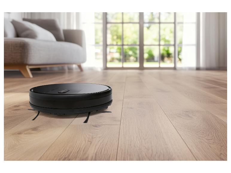 Aspirateur robot noir sur parquet dans un salon lumineux.