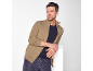 Homme en veste zippée beige et t-shirt bleu marine, appuyé sur un cube blanc.