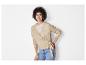 Une femme porte un pull beige à boutons et un jean bleu.