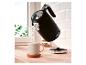 Bouilloire noire versant de l'eau chaude dans une tasse sur un comptoir en bois.
