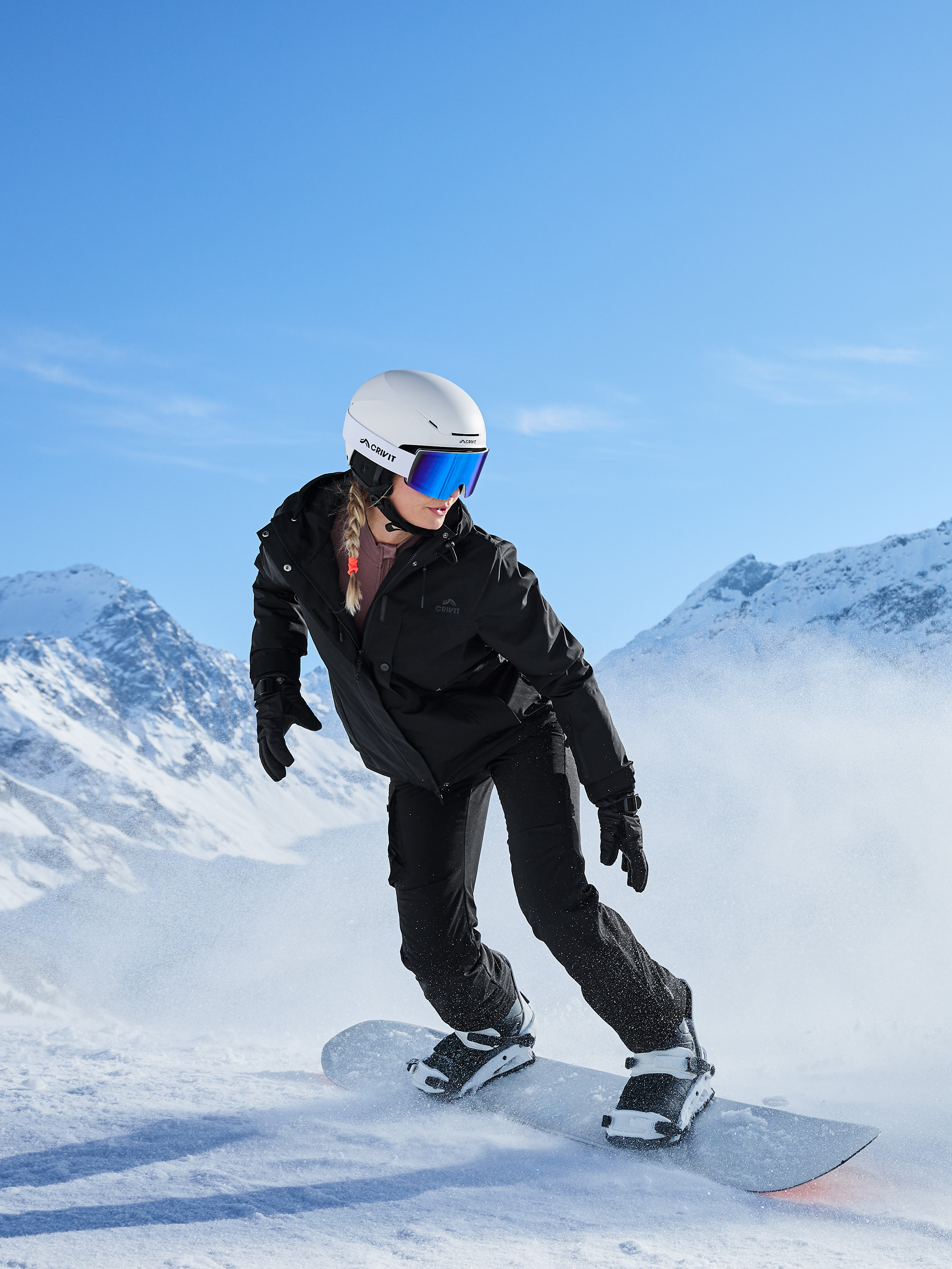Snowboardeuse en veste et pantalon de ski noirs, casque blanc et lunettes de ski bleues sur la piste