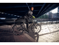 Homme en tenue de sport avec un vélo sous un pont, cadre urbain.