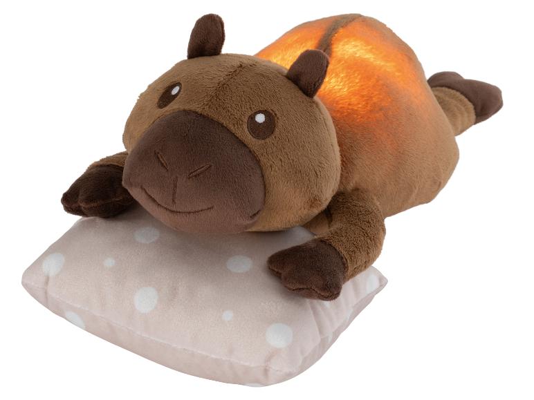 Veilleuse capybara en peluche marron sur un oreiller à pois.