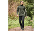 Un homme avec une veste en polaire verte et un pantalon noir se promène dans une forêt