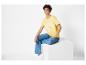 Une femme porte un t-shirt jaune avec l'inscription 'Good Vibes Only' et un jean bleu.