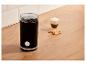 Moulin à café noir avec grains, café et biscuits sur un comptoir en bois.