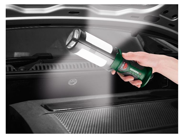 Une main tient une lampe de travail verte et noire, éclairant le compartiment moteur d'une voiture.