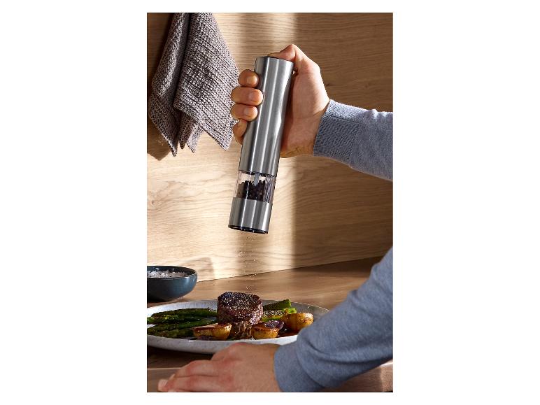 Main assaisonnant un plat de bœuf et d'asperges avec un moulin à poivre électrique.