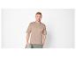 Homme en t-shirt beige et pantalon vert, tenant un sweat-shirt gris.