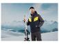 Homme en tenue de ski avec des skis devant un paysage montagneux.