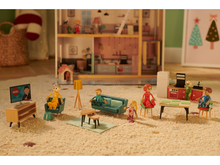 Maison de poupée avec figurines familiales miniatures, meubles et une télévision diffusant les actualités.
