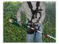 Homme avec coupe-bordure sans fil et harnais, taillant un buisson vert.