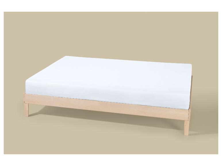 Un matelas blanc sur un cadre de lit en bois clair sur fond beige.