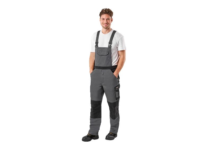 Homme souriant portant une salopette de travail grise et un t-shirt blanc.