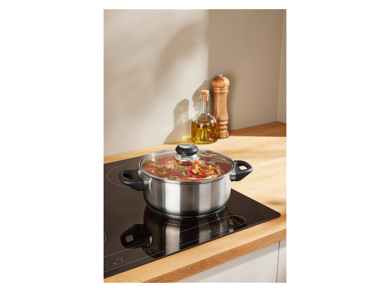 Une casserole en acier inoxydable avec couvercle mijote une soupe sur une plaque de cuisson à induction.