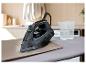 Fer à repasser noir sur une planche à repasser avec un verre d'eau.