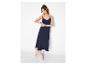 Femme en robe longue bleu marine et baskets beiges, appuyée contre un mur blanc.