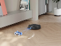 Aspirateur robot noir évitant un jouet sur un parquet en bois.