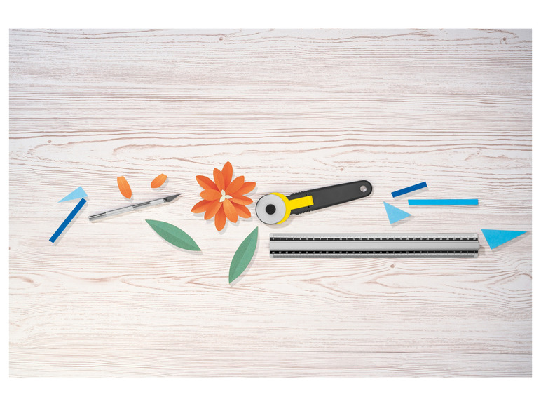 Un tapis de coupe, un cutter rotatif et une fleur en papier sur une table en bois.