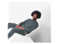 Un homme assis sur un cube blanc, vêtu d'un sweat-shirt et d'un pantalon de survêtement gris foncé.