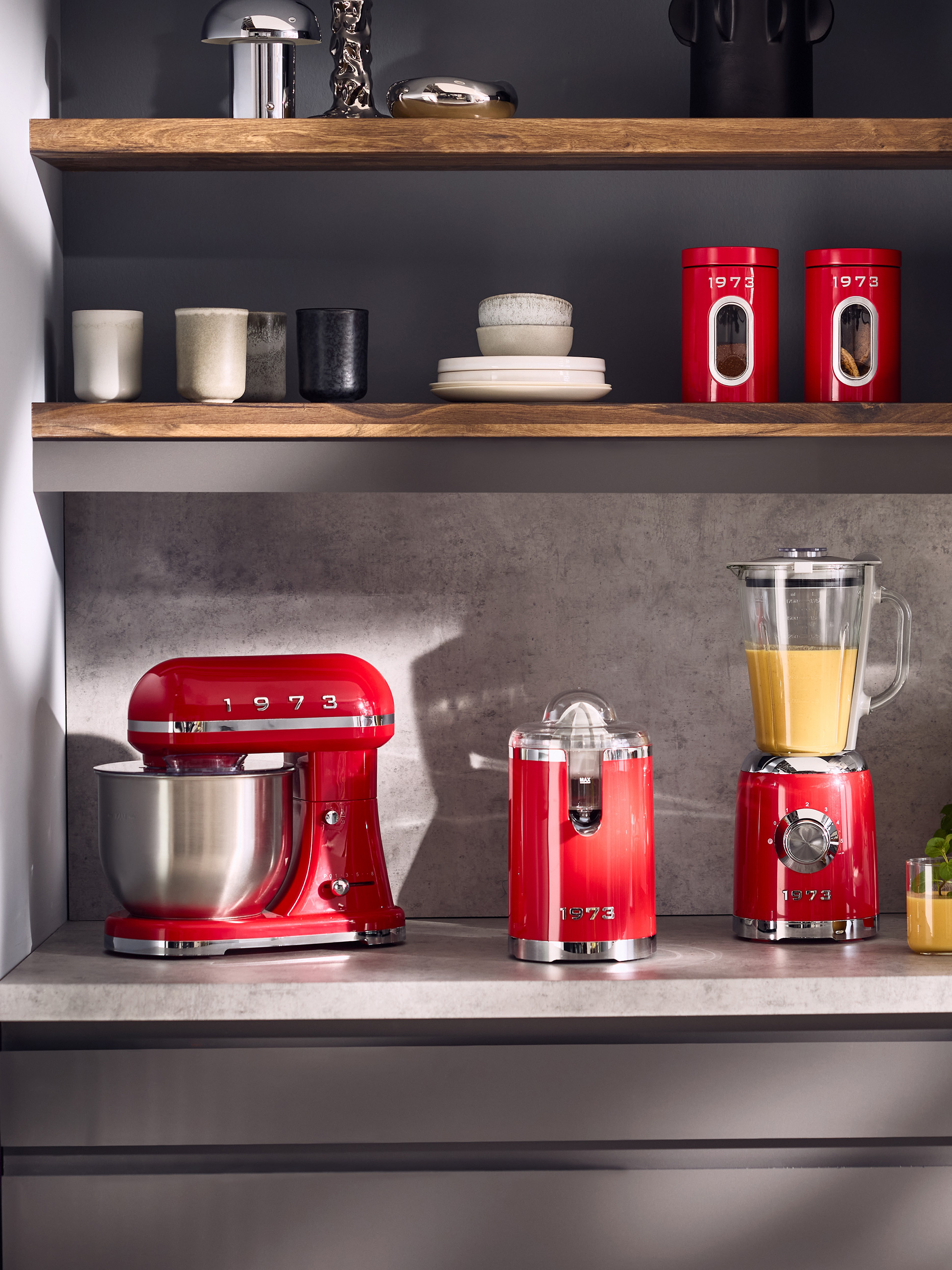Robot pâtissier rouge, presse-agrumes et mixeur sur le comptoir, avec des boîtes rouges sur l'étagère.