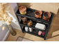 Étagère de rangement noire à 3 niveaux avec des articles de cuisine comme des bocaux, des tasses et un beurrier.