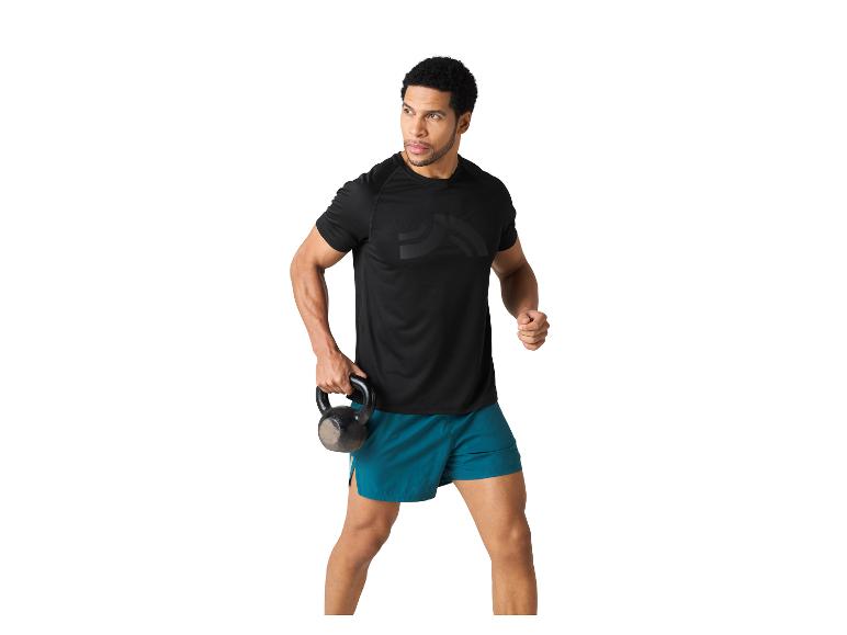 Un homme en t-shirt noir et short turquoise tient un kettlebell.