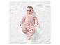 Bébé portant un pyjama rose à motifs animaux sur un plaid blanc.