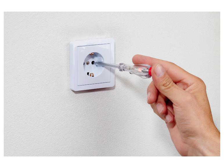 Main tenant un testeur de tension dans une prise électrique.