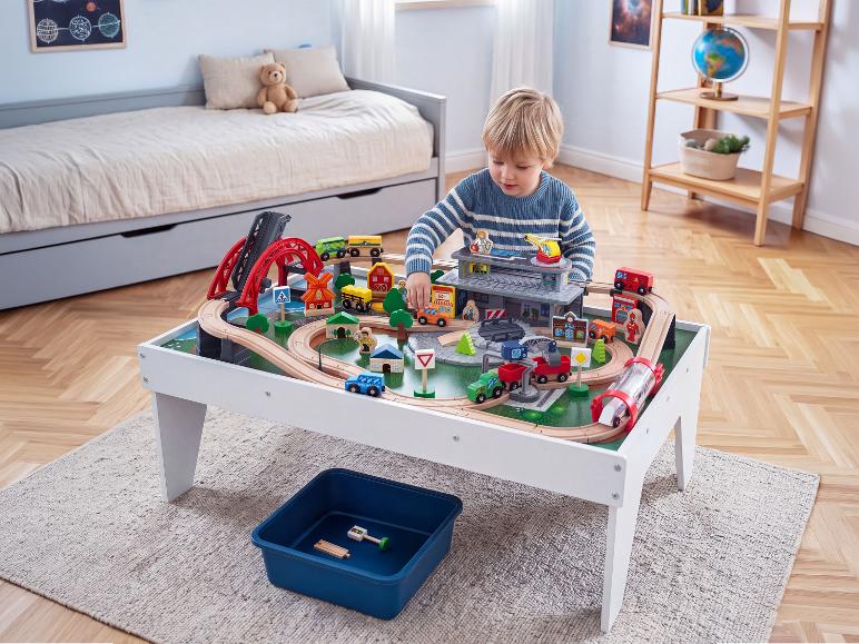 Garçon jouant avec une table de train en bois avec ponts et bâtiments dans une chambre d'enfant.
