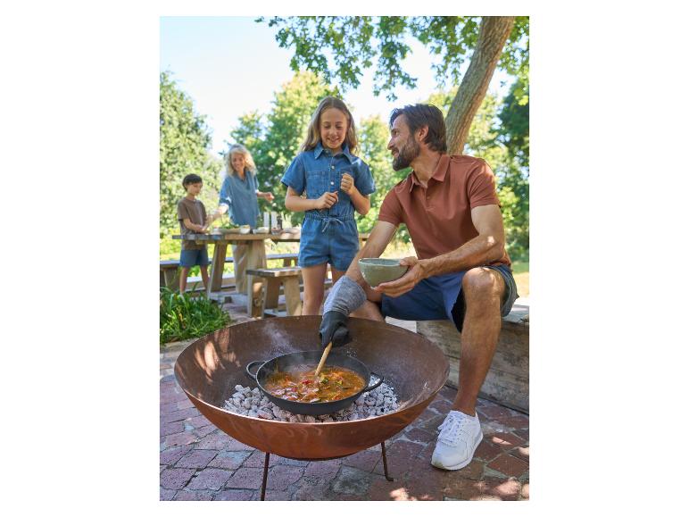 Famille cuisinant un ragoût dans une marmite en fonte sur un brasero dans le jardin.