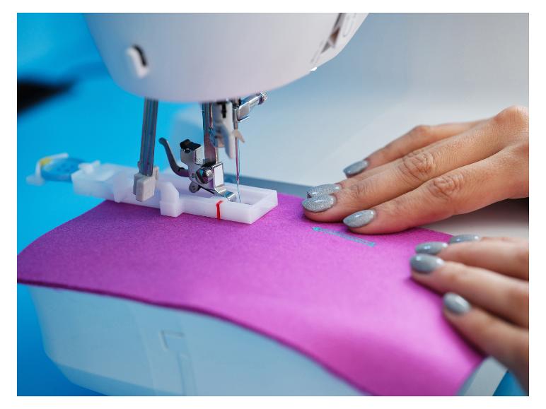 Machine à coudre avec tissu violet et mains de femme