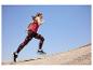 Femme courant en débardeur rouge et leggings à motifs sur fond de ciel bleu.