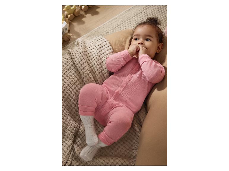 Bébé en grenouillère rose allongé sur une couverture tricotée, avec des jouets en bois en arrière-plan.