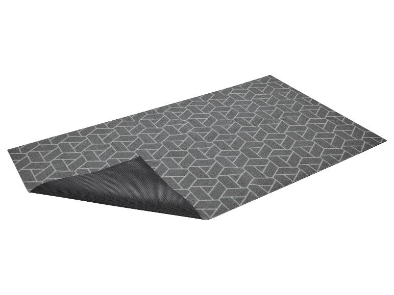 Tapis gris à motif géométrique, partiellement soulevé, montrant le dessous.