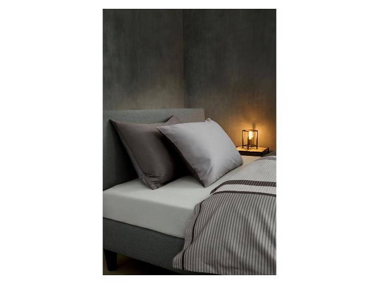 Chambre à coucher avec lit gris, deux oreillers et housse de couette rayée, avec une lampe de chevet.