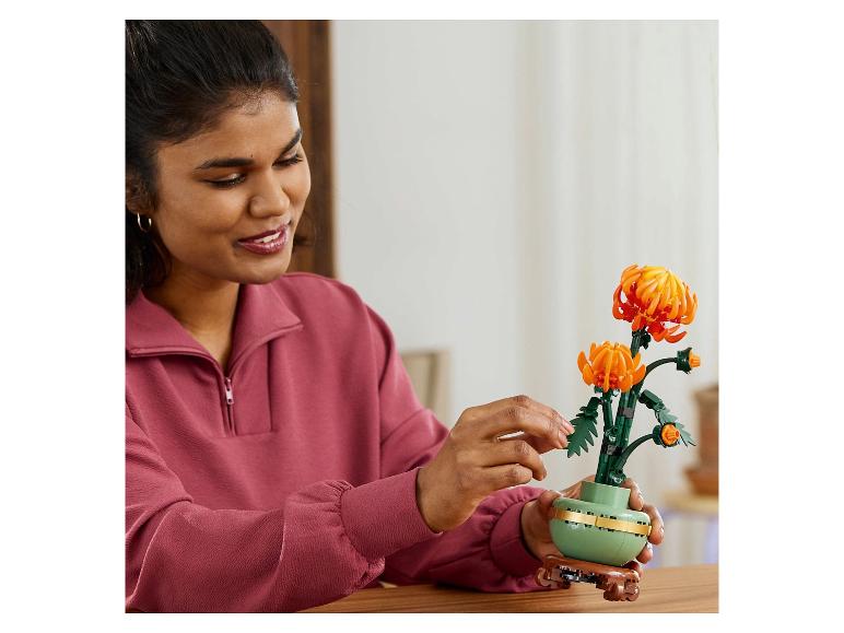 Une femme souriante arrange une fleur LEGO orange dans un vase vert.