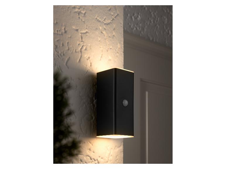 Un luminaire mural rectangulaire noir avec capteur de mouvement éclaire un mur texturé.