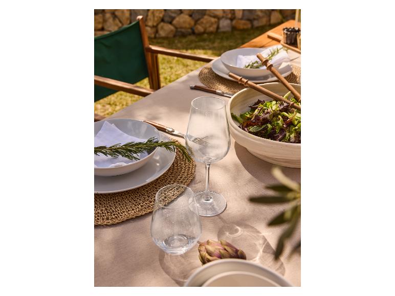 Table de repas en plein air avec assiettes, couverts et verres à vin.