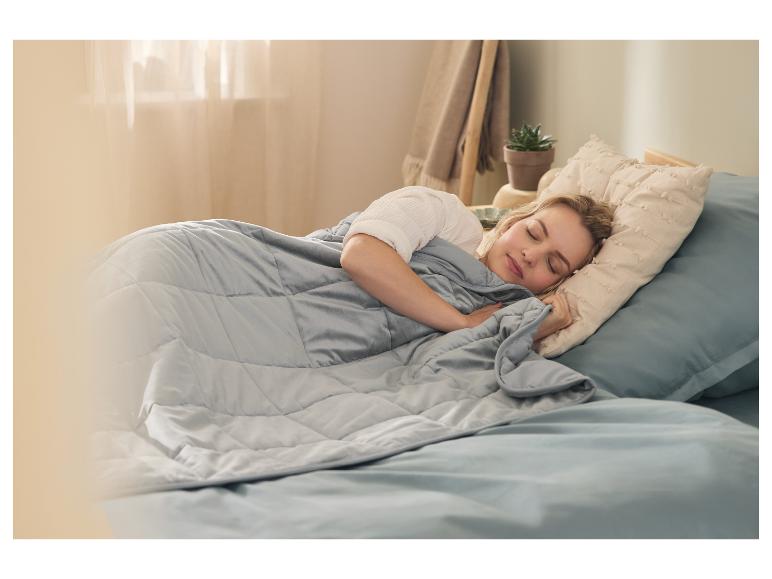 Femme dormant paisiblement dans son lit sous une couverture lestée grise.
