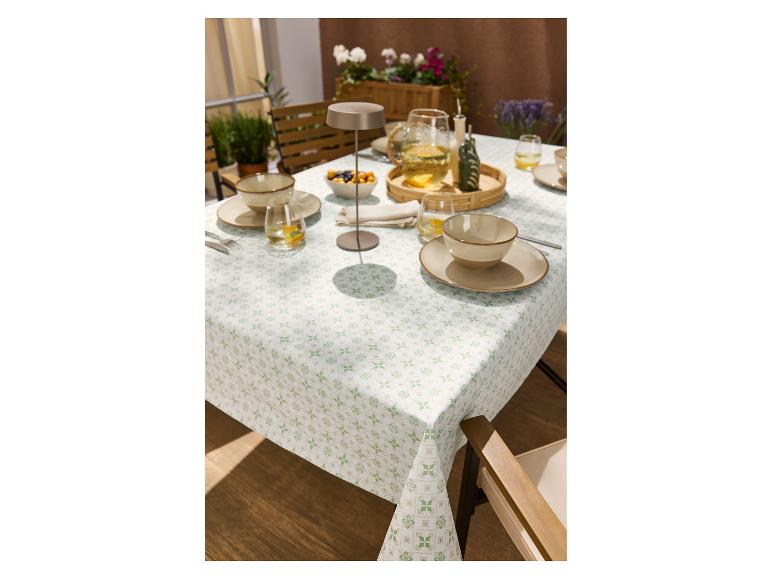 Nappe à motif vert et beige, dressée avec vaisselle et boissons en extérieur.